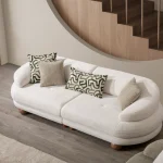 Premium sand grey curved sofa with sculptural round wooden legs and decorative cushions