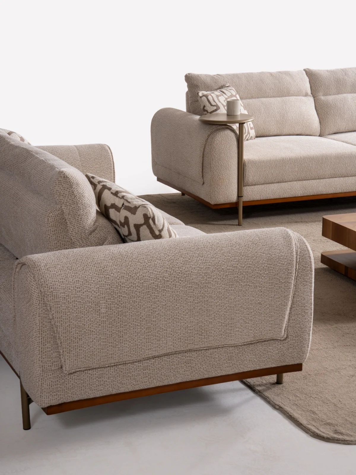 A modern textured fabric sofa featuring rounded armrests, adjustable horizontal back cushions, a dark wood plinth base, and a sleek integrated metallic side tray table in a minimalist living room setting.