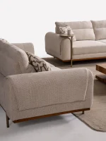 A modern textured fabric sofa featuring rounded armrests, adjustable horizontal back cushions, a dark wood plinth base, and a sleek integrated metallic side tray table in a minimalist living room setting.