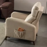 A high-back recliner-style accent armchair with soft neutral upholstery, cushioned head support, integrated side storage pocket, and dark tapered wooden legs, shown in a modern interior setting.