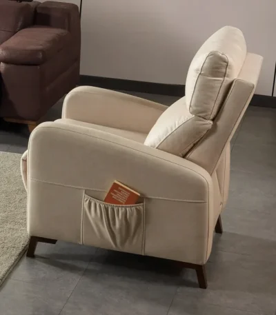 A high-back recliner-style accent armchair with soft neutral upholstery, cushioned head support, integrated side storage pocket, and dark tapered wooden legs, shown in a modern interior setting.
