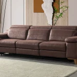 A modern multi-seater recliner sofa featuring adjustable headrests, extendable footrests, wide plush armrests, and a rich textured leatherette finish in a contemporary living room setting.