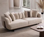 Sola Sofa featuring rounded armrests, plush back cushions, and a wooden base trim in a modern living room setting.