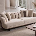 Sola Sofa featuring rounded armrests, plush back cushions, and a wooden base trim in a modern living room setting.