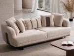 Sola Two Seater Sofa featuring rounded armrests, plush back cushions, and a wooden base trim in a modern living room setting.