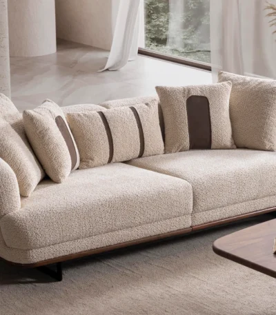 Sola Two Seater Sofa featuring rounded armrests, plush back cushions, and a wooden base trim in a modern living room setting.