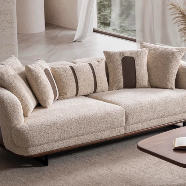 Sola Two Seater Sofa featuring rounded armrests, plush back cushions, and a wooden base trim in a modern living room setting.