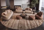 Tolia Sofa Set featuring a modular curved sofa, sculptural armchair, matching ottomans, and coffee tables arranged on a large round patterned rug in a modern living room.