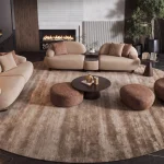 Tolia Sofa Set featuring a modular curved sofa, sculptural armchair, matching ottomans, and coffee tables arranged on a large round patterned rug in a modern living room.