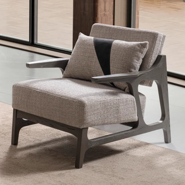 A contemporary Nova Armchair featuring an architectural open wooden frame, slim contoured armrests, a deep plush seat cushion, and a matching geometric accent pillow in a sunlit room setting.