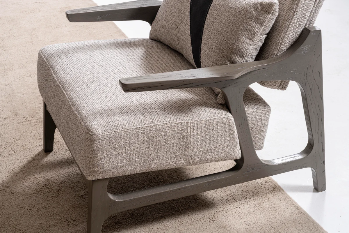 A contemporary accent armchair featuring an architectural open wooden frame, slim contoured armrests, a deep plush seat cushion, and a matching geometric accent pillow in a sunlit room setting.