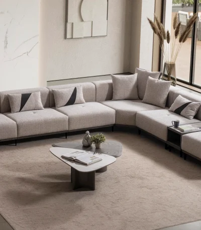 A modern modular Nova Corner Sofa featuring generous deep seating, multiple plush backrest cushions, geometric accent pillows, an ottoman extension, and low-profile metal legs against a plain white background.
