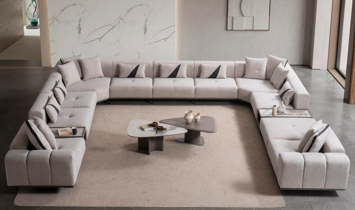 An extra-large U-shaped modular sectional sofa featuring expansive seating, plush backrest cushions, geometric accent pillows, and integrated tray console modules in a luxurious modern interior.