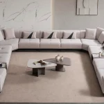An extra-large U-shaped modular sectional sofa featuring expansive seating, plush backrest cushions, geometric accent pillows, and integrated tray console modules in a luxurious modern interior.