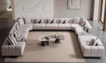 An extra-large U-shaped modular sectional sofa featuring expansive seating, plush backrest cushions, geometric accent pillows, and integrated tray console modules in a luxurious modern interior.