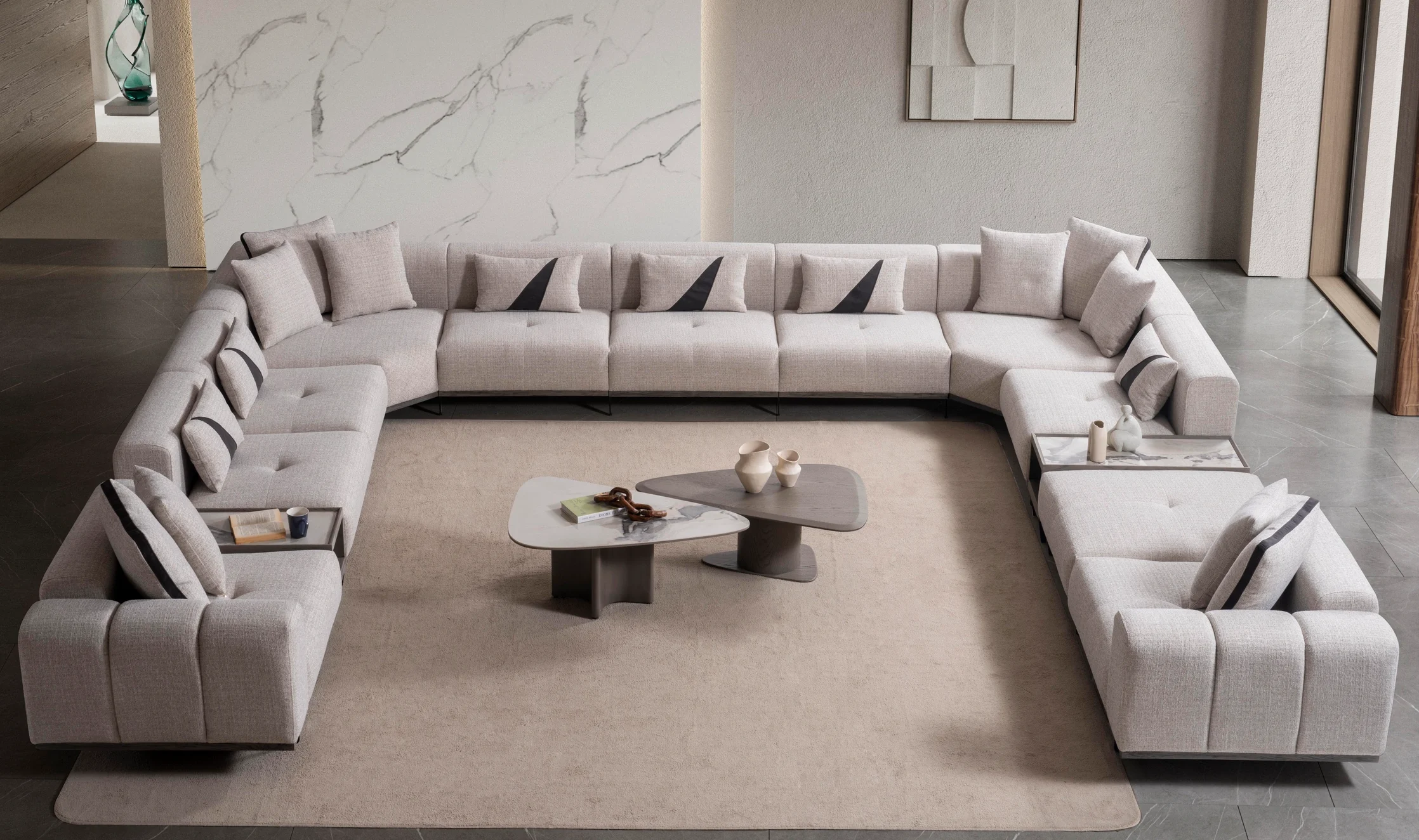 nova-xl-corner-sofa-05 An extra-large U-shaped modular sectional sofa featuring expansive seating, plush backrest cushions, geometric accent pillows, and integrated tray console modules in a luxurious modern interior.